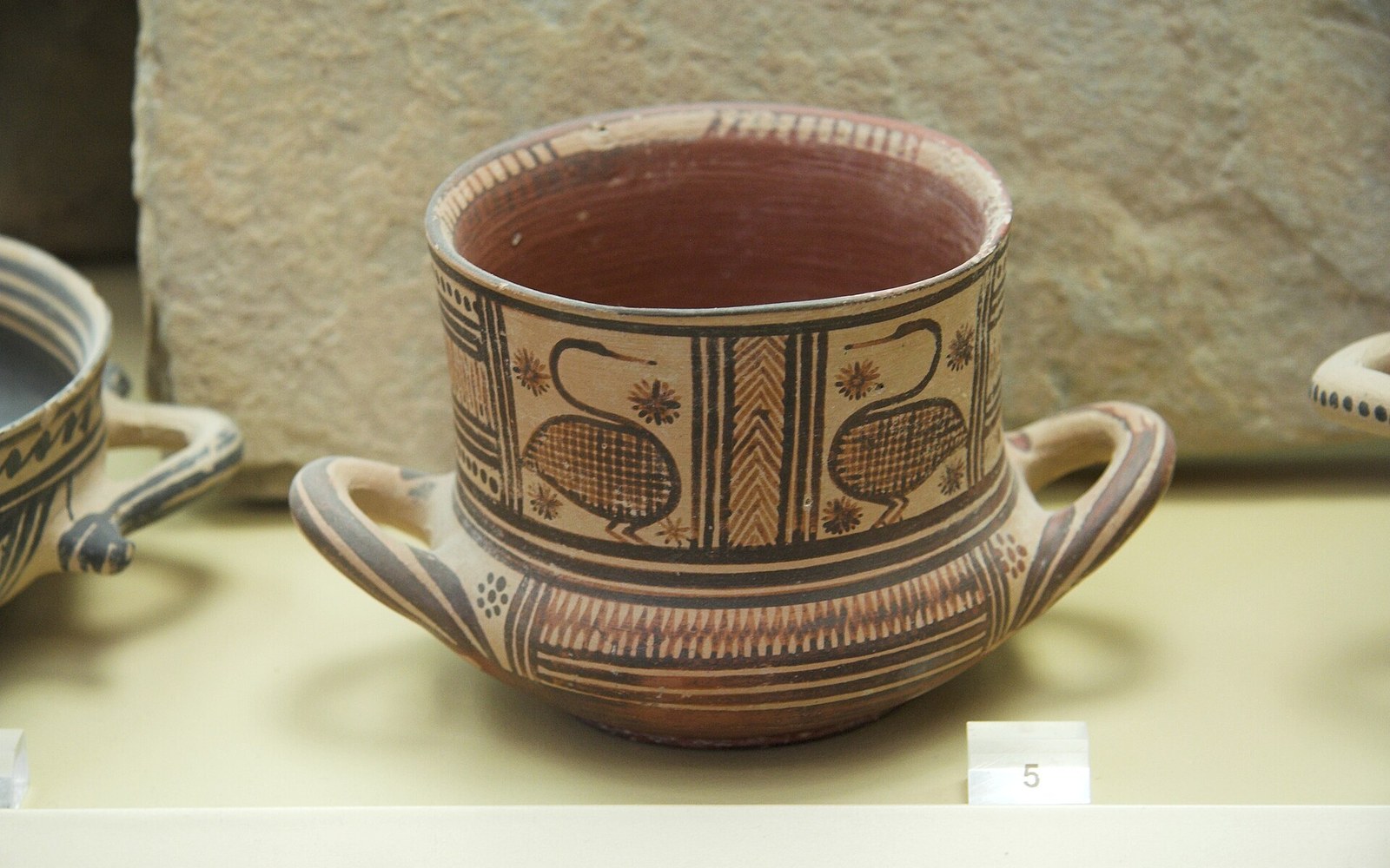 Ancient Greek two-handled cup painted with geometric bird motifs, displayed in a museum case
